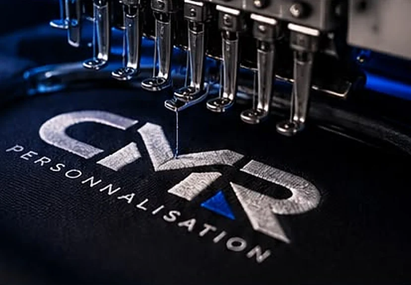 Machine à broder en train de réaliser le logo CMR Personnalisation sur un textile noir
